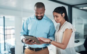 Cropped shot of two businesspeople standing together in the office and using a tablet for looking into their tax file